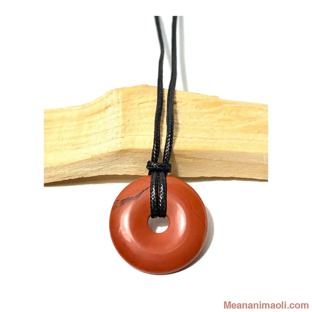 Pendentif donut en Jaspe Rouge naturel suspendu par un cordon en coton ciré noir devant un morceau de bois de Palo Santo - MEANANIMAOLI