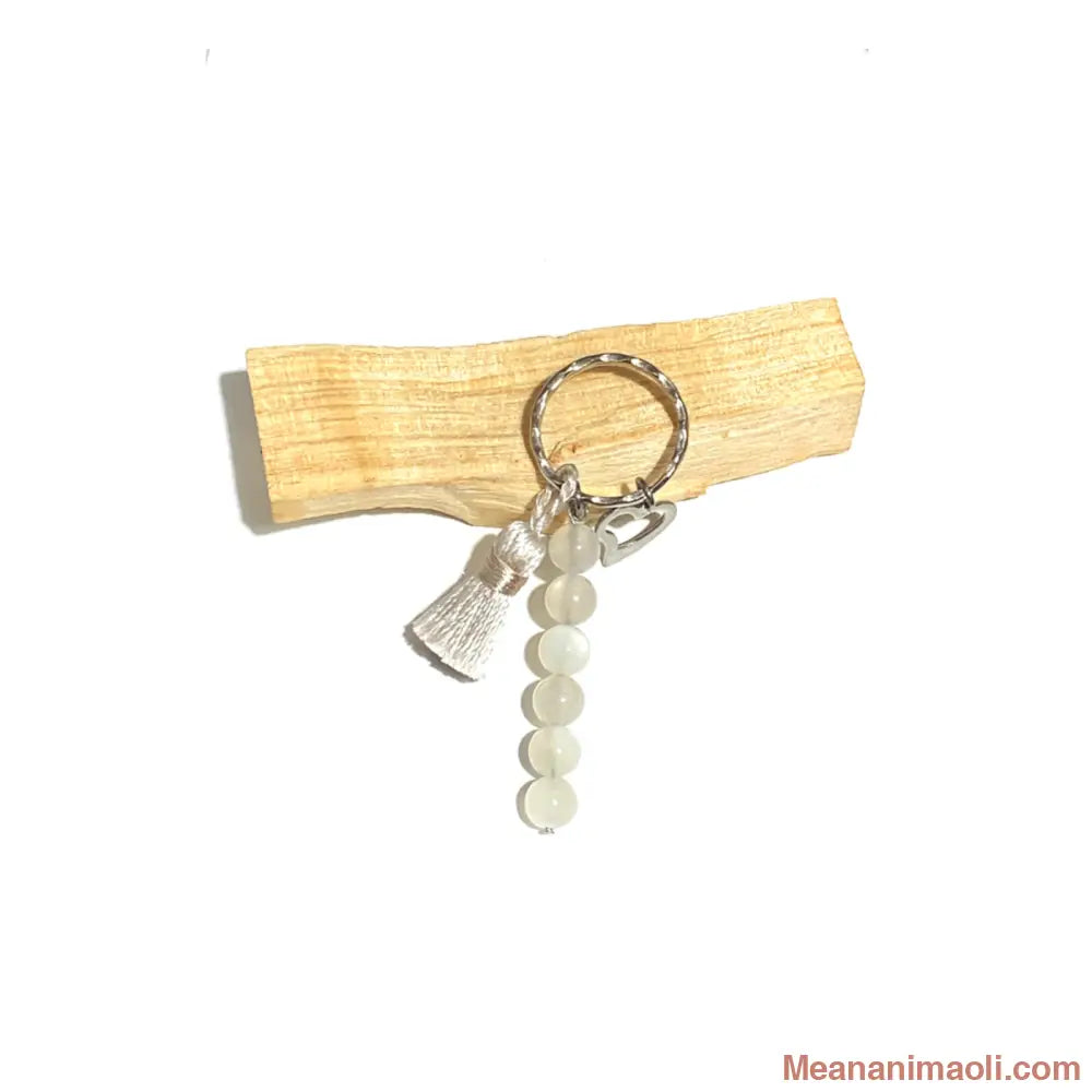 Porte-clés en perles de Pierre de Lune blanche (8 mm) avec un pompon écru et une breloque cœur en acier inoxydable. Accessoire énergétique MEANANIMAOLI.