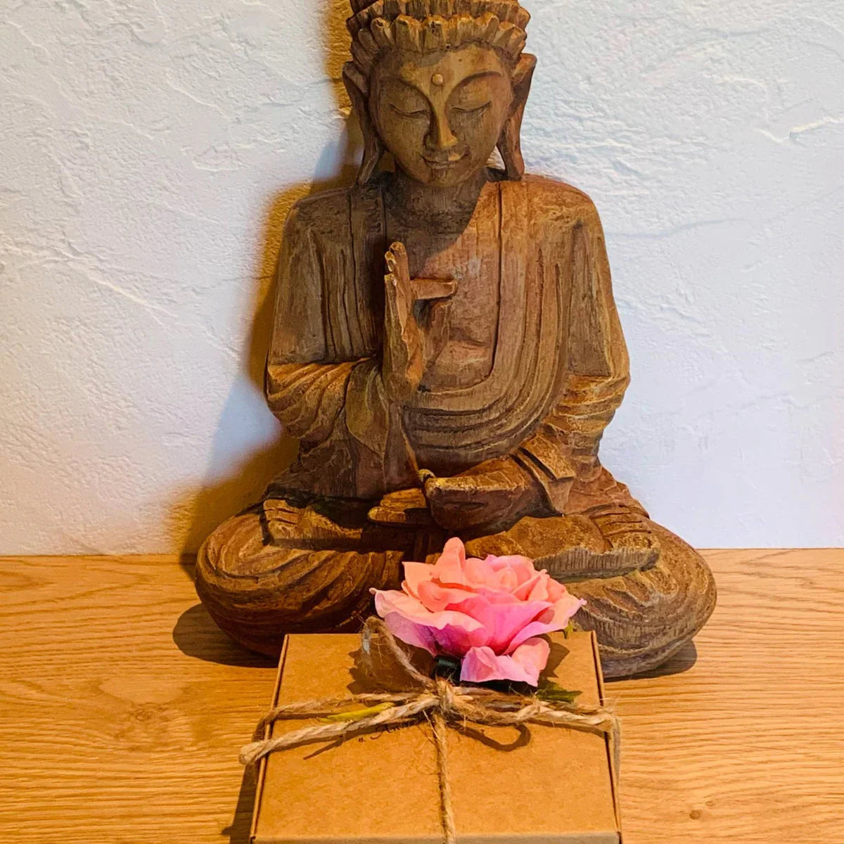 Statue de Bouddha en bois avec une boîte cadeau (box) posée à côté, symbolisant la sérénité et le bien-être. Idées cadeaux lithothérapie et pierres naturelles.