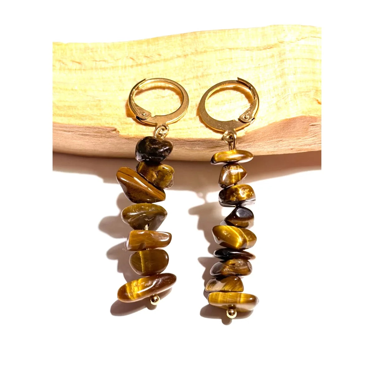 Boucles d'oreilles pendantes en acier inoxydable doré avec perles chips d'Oeil de Tigre naturel posées sur un morceau de bois Palo Santo, une création MEANANIMAOLI