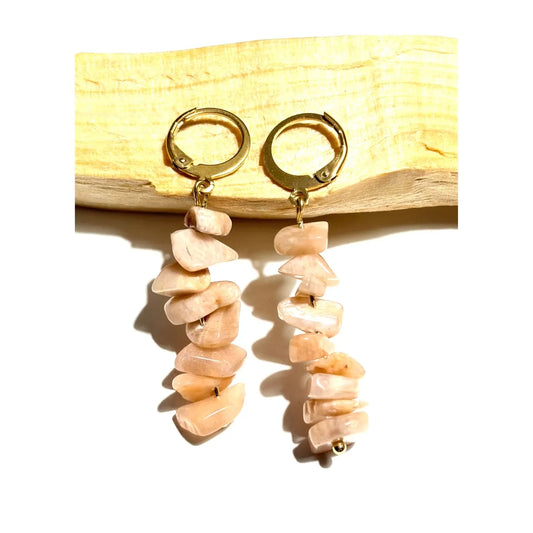 Boucles d'oreilles pendantes en acier inoxydable doré avec perles chips de Pierre du Soleil naturelle posées sur un morceau de bois Palo Santo, une création MEANANIMAOLI
