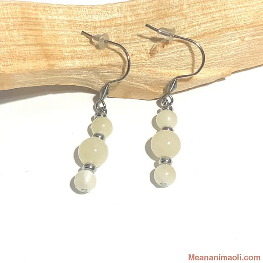 Paire de boucles d'oreilles en acier inoxydable argenté avec pierre naturelle Jade Jaune, posées sur un bâton de Palo Santo