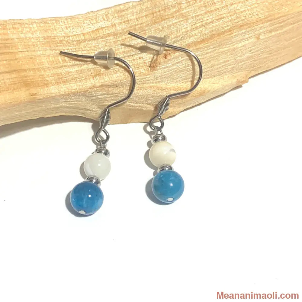 Paire de boucles d'oreilles en acier inoxydable argenté avec perles de Nacre et Apatite naturelle, posées sur un bâton de Palo Santo