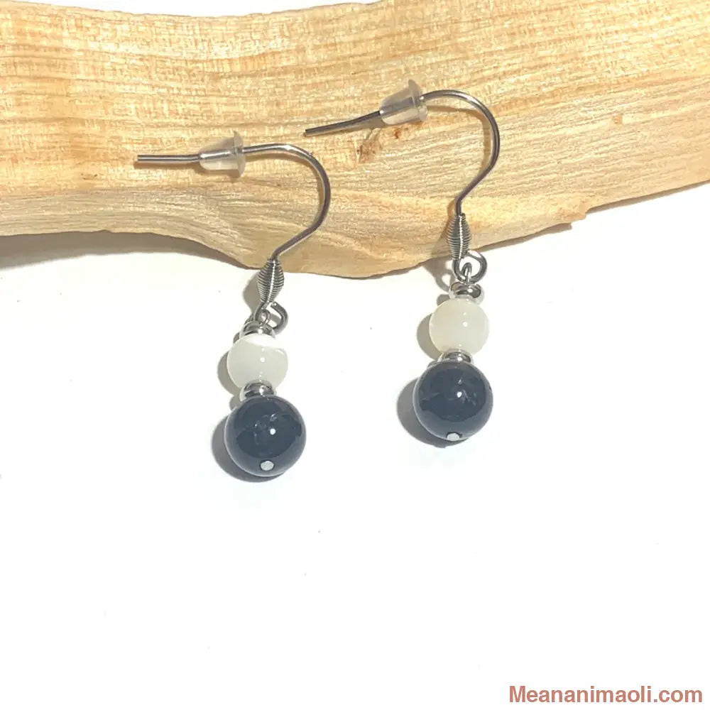 Paire de boucles d'oreilles en acier inoxydable argenté avec perles de Nacre et Tourmaline Noire naturelle, posées sur un bâton de Palo Santo