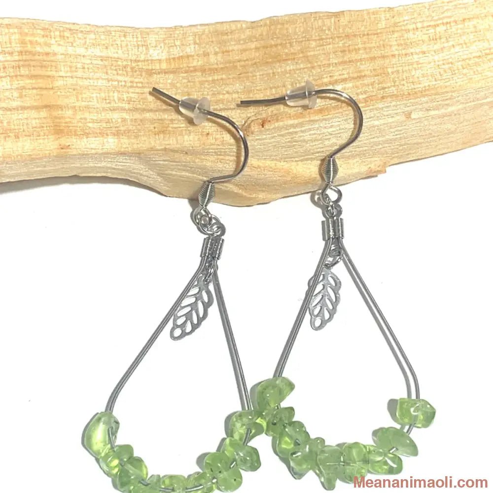 Paire de boucles d'oreilles en acier inoxydable argenté avec pierre naturelle Péridot, posées sur un bâton de Palo Santo