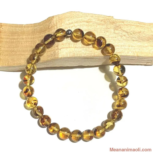 Bracelet en perles d'Ambre naturelle (6mm) et perle en acier inoxydable argenté, posé sur un bâton de palo santo.