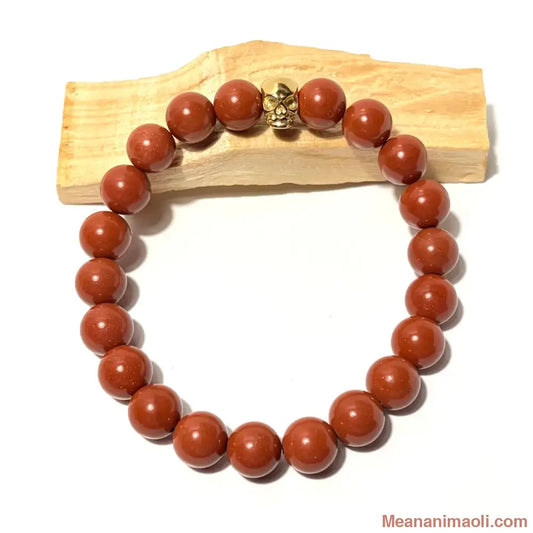 Bracelet en perles de 10 mm Jaspe Rouge naturelle et tête de mort en acier inoxydable doré posé sur un bois palo santo