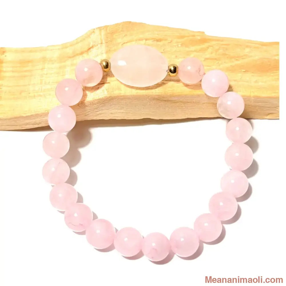 Bracelet de lithothérapie en perles de Quartz Rose de 8 mm avec perle centrale ovale, posé sur du bois de Palo Santo, boutique MEANANIMAOLI.