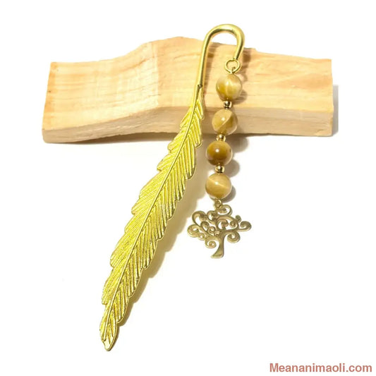 Marque-page plume dorée avec perles d'œil de tigre marron et doré et une breloque arbre de vie, posé sur un support en bois