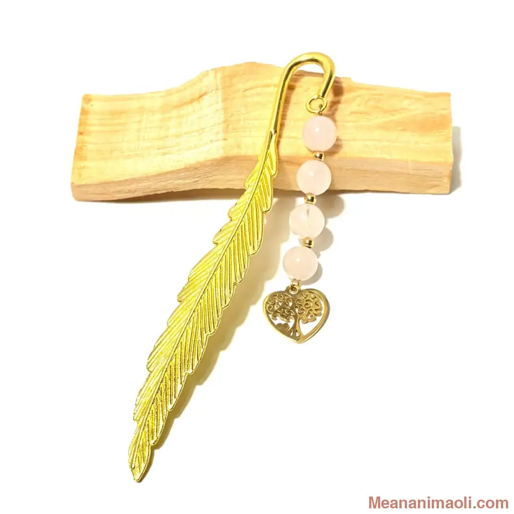 Marque-page plume doré avec quatre perles de quartz rose et une breloque coeur fleur de vie, posé sur un support en bois clair