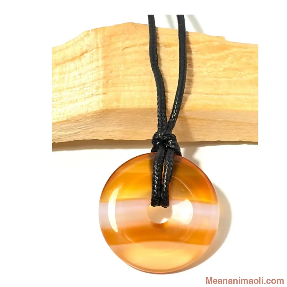 Pendentif donut en Cornaline naturelle aux bandes orange et blanches translucides suspendu par un cordon en coton ciré noir devant un morceau de bois de Palo Santo - MEANANIMAOLI