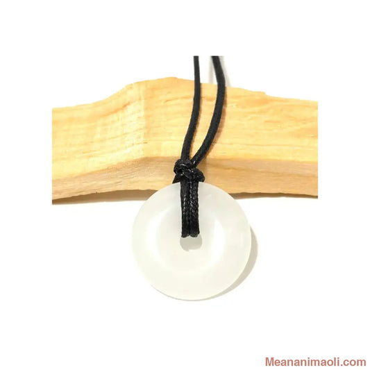 Pendentif donut en Cristal de Roche naturel blanc translucide suspendu par un cordon en coton ciré noir devant un morceau de bois de Palo Santo - MEANANIMAOLI