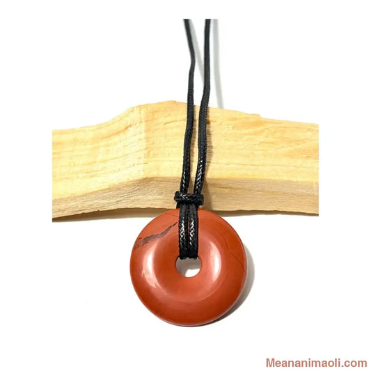 Pendentif donut en Jaspe Rouge naturel suspendu par un cordon en coton ciré noir devant un morceau de bois de Palo Santo - MEANANIMAOLI