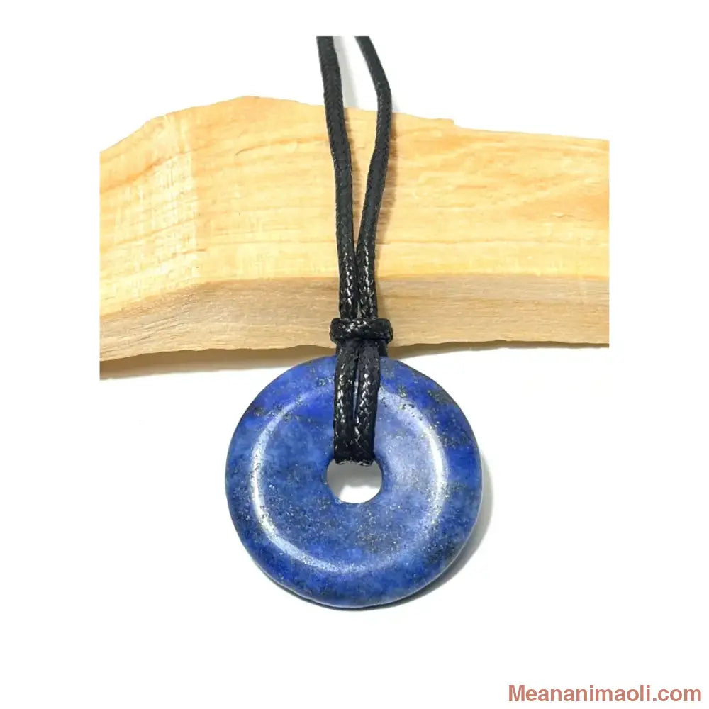 Pendentif donut en Lapis Lazuli naturel bleu profond  suspendu par un cordon noir devant un morceau de bois de Palo Santo - MEANANIMAOLI
