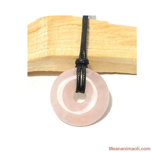 Pendentif donut en Quartz Rose suspendu par un cordon en coton ciré noir devant un morceau de bois de Palo Santo - MEANANIMAOLI