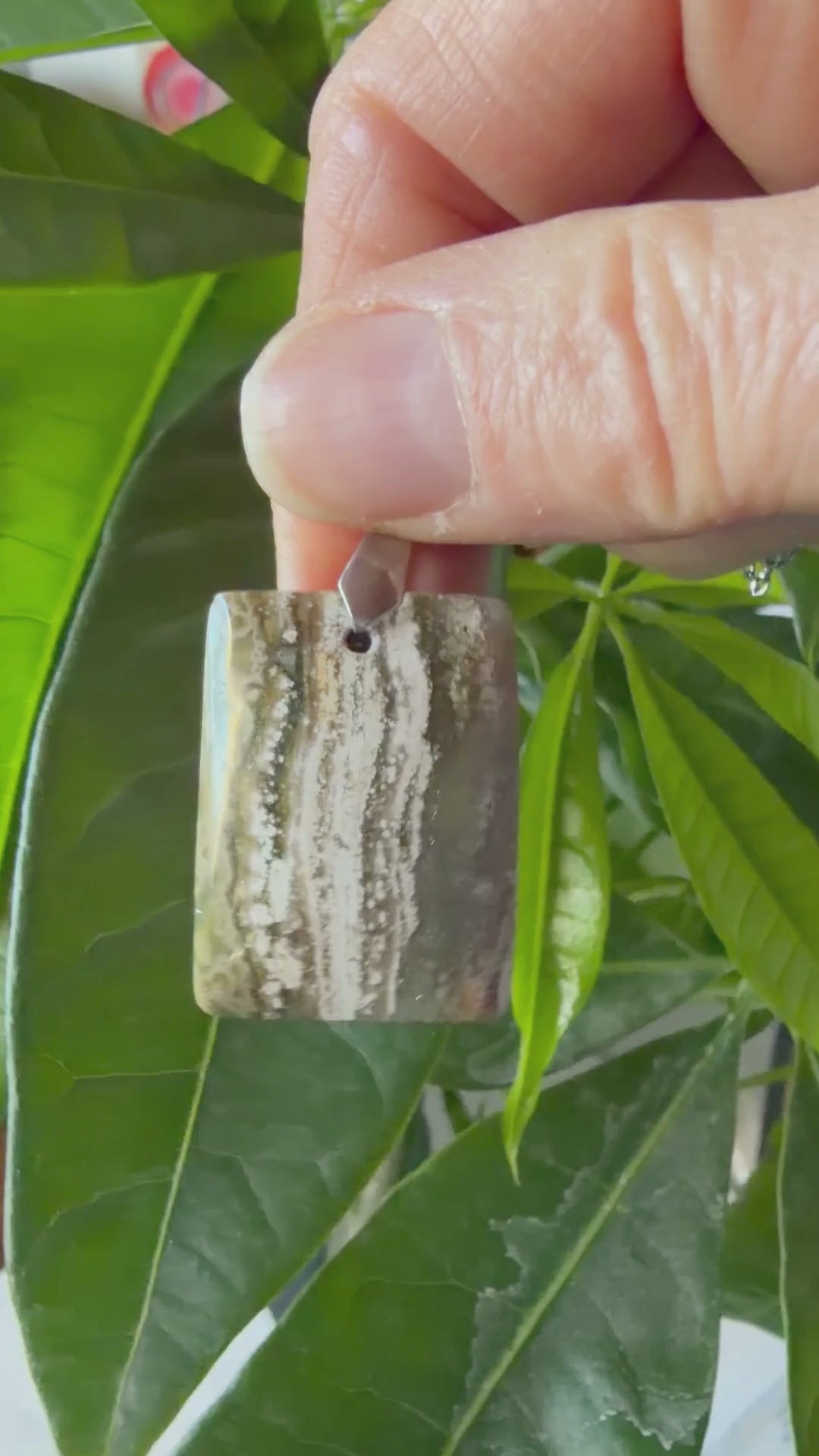 Vidéo d'un collier en Jaspe Océan naturel de forme rectangulaire, monté sur une chaîne en acier inoxydable. La vidéo met en valeur les motifs organiques verts et blancs uniques et les détails de la pierre par MEANANIMAOLI
